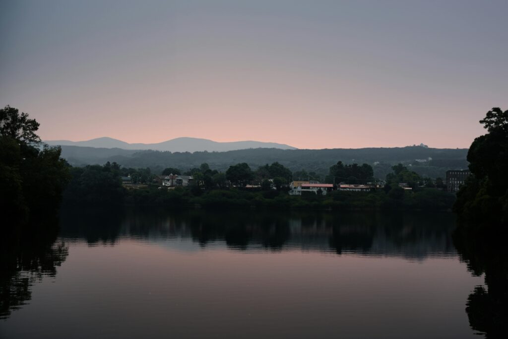 Photo of Lake Oswego, showcasing its serene waters surrounded by lush greenery and upscale homes. The image captures the tranquil beauty of the lake, with reflections of trees and buildings shimmering on the water’s surface. The picturesque setting highlights the peaceful, residential charm of the area.