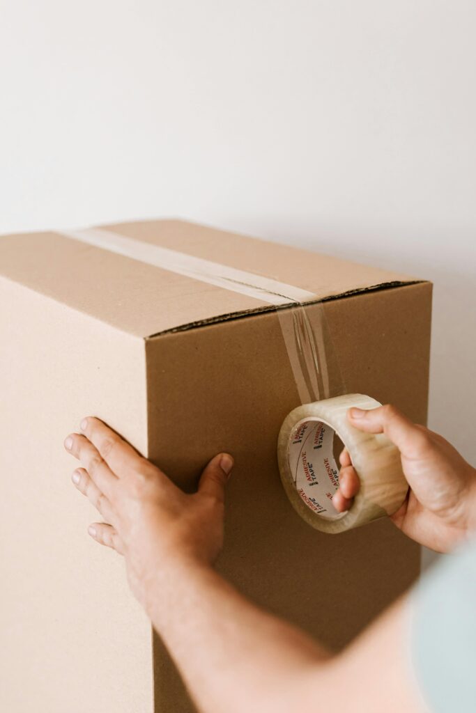 Photo of a box being taped closed, with a hand applying packing tape to securely seal the box. The image emphasizes the attention to detail and care involved in the packing process, highlighting the moving company's commitment to protecting belongings during transit.