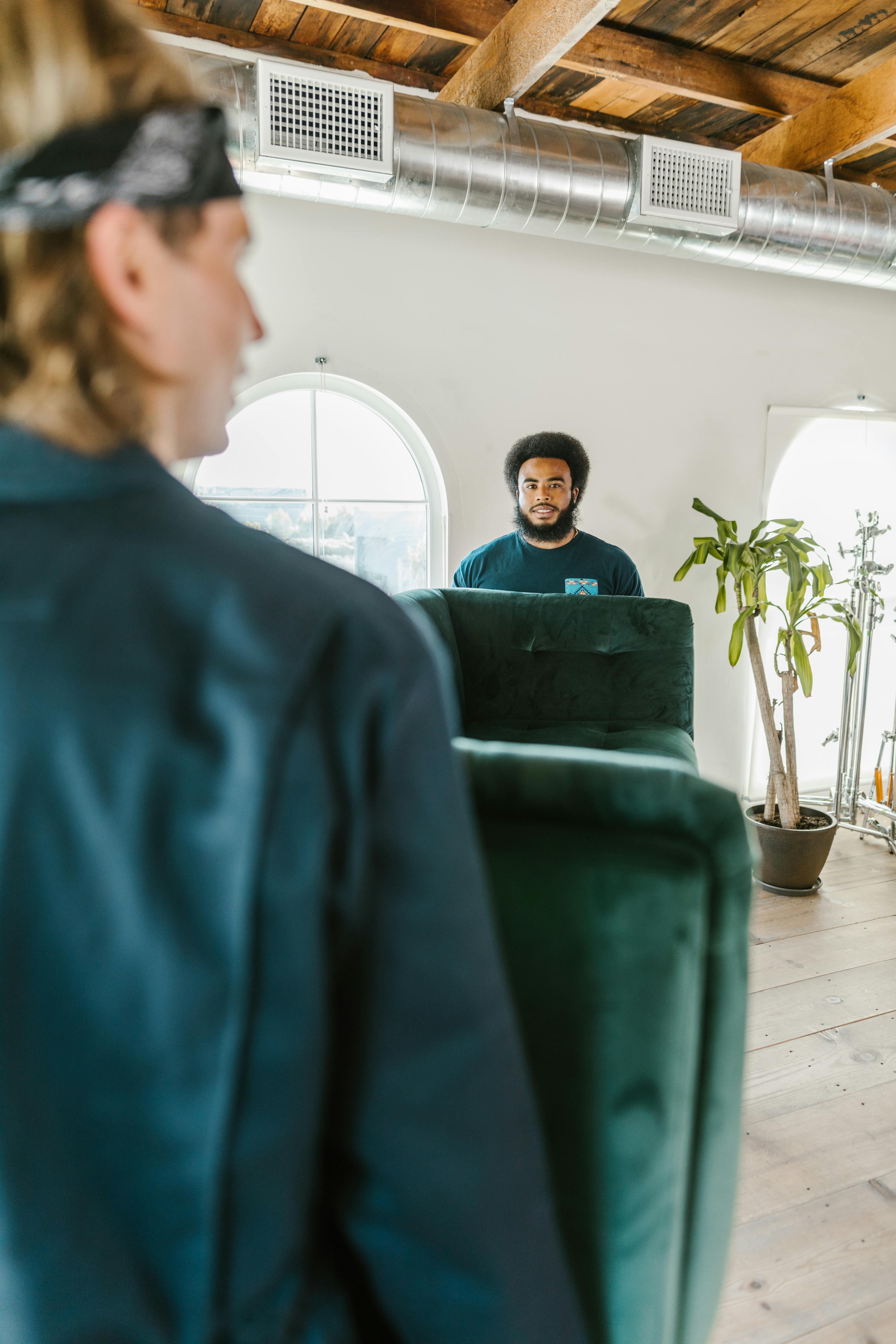 Photo of two movers carefully maneuvering a couch through a doorway. The movers are working together, using proper techniques to ensure the couch is handled safely and efficiently. The image highlights the teamwork and professionalism of the moving company in managing large furniture during a move.